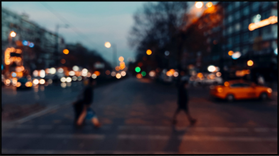 a blurred image of city traffic with people walking or crossing a zebra line, representing urban movement and activity.