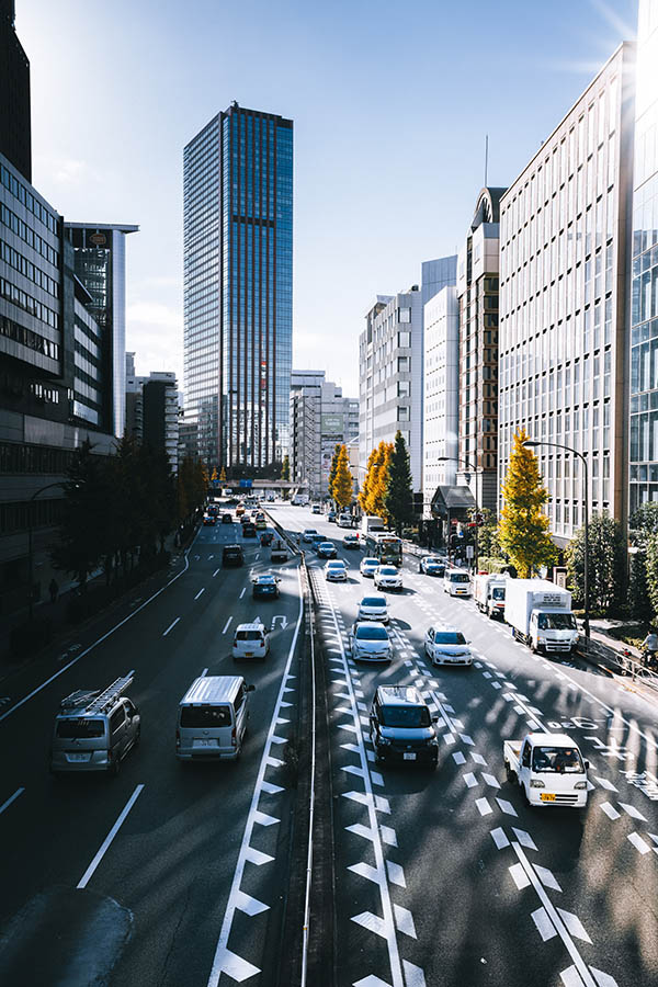 a city backdrop with a four-lane road and multiple cars driving, showcasing congestion charging solutions for urban traffic management.