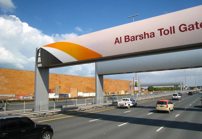 multiple cars driving under a toll gate with a banner reading 'al barsha toll gate,' showcasing automatic toll collection solutions.